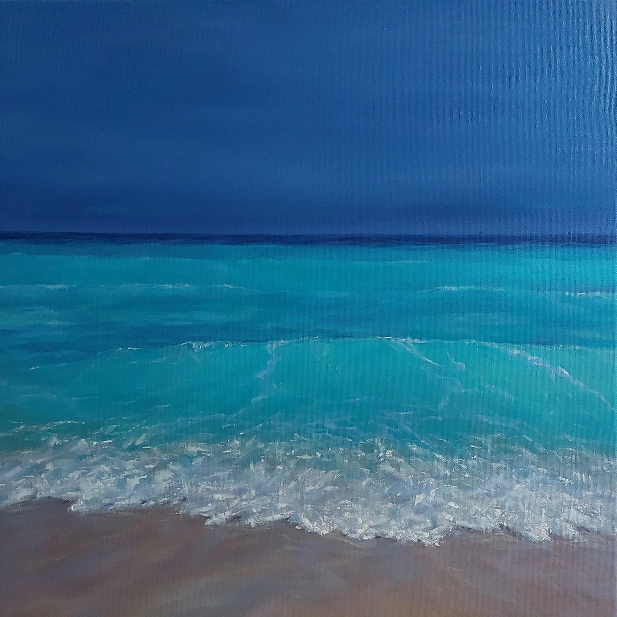 A turquoise wave breaking on the sand under a deep blue sky